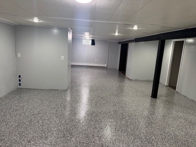 Empty basement with gray walls, speckled gray floor, black support beams, and recessed lighting.