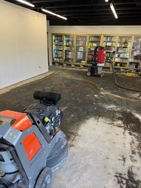Concrete floor being ground with machinery in a store. White wall, shelves of items in background.