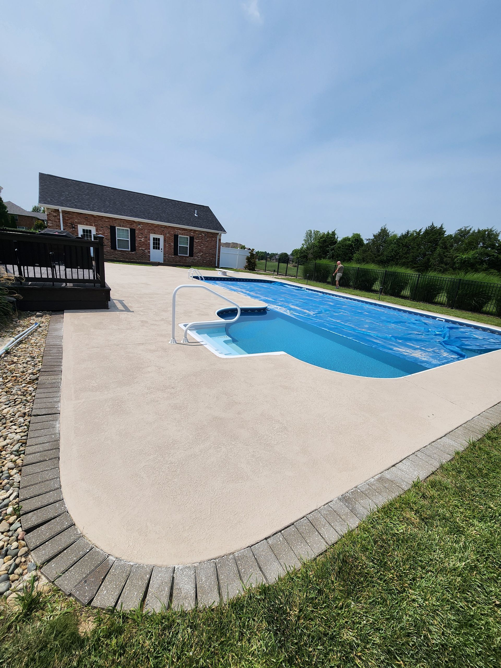 Backyard with a swimming pool, blue water, and tan concrete patio. Brick house and green grass surround.