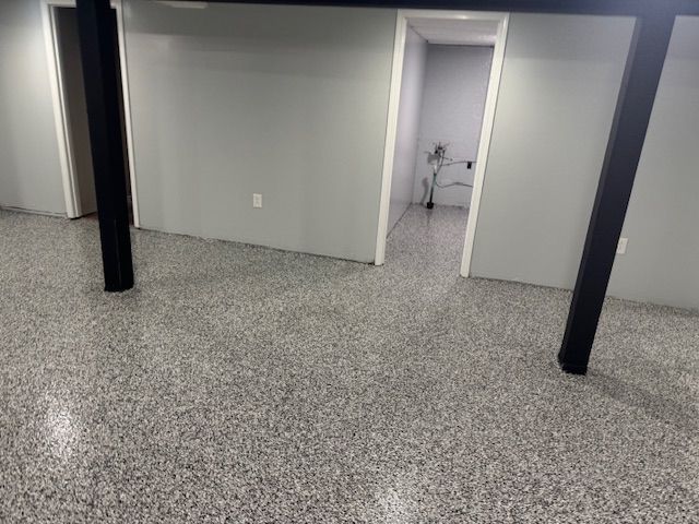 Finished basement with gray epoxy floor, gray walls, black support beams, and white doorways.