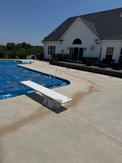 Pool with diving board and blue cover; white house in background.
