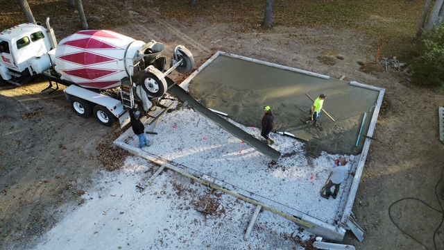 Concrete truck pouring cement into a rectangular form. Three workers use tools to spread the cement.