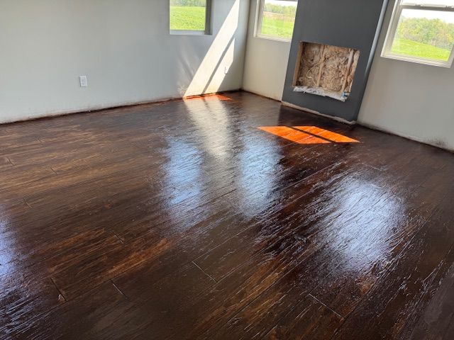 Newly stained and glossy dark brown hardwood floor in a room with a fireplace, windows, and light gray walls.