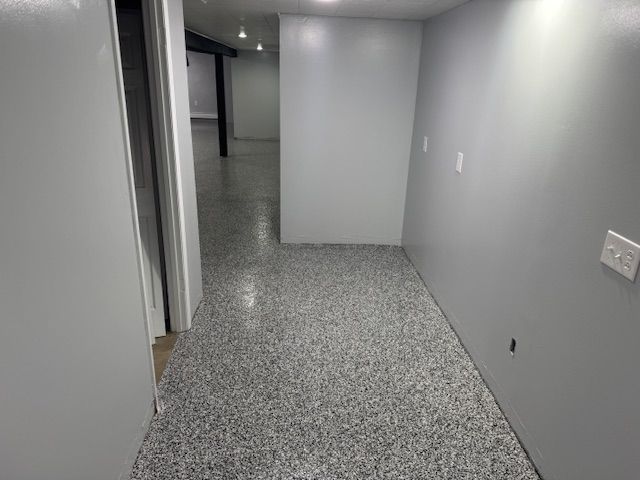 Gray-painted basement hallway with speckled flooring, doorways, and electrical outlets.