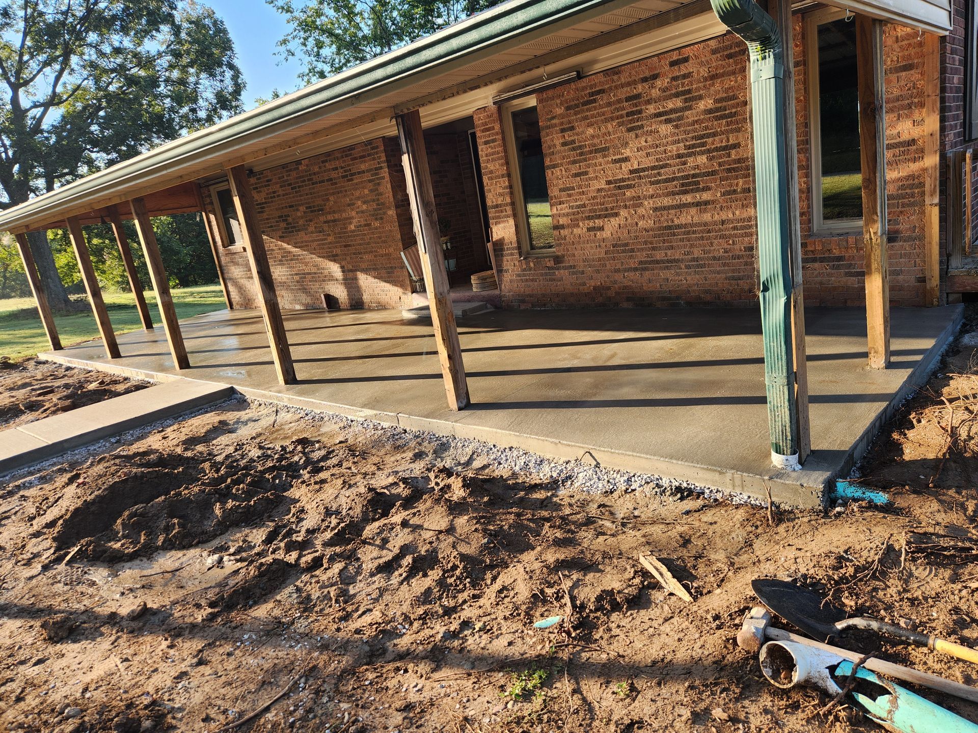 A newly poured concrete patio with wooden supports adjacent to a brick building.