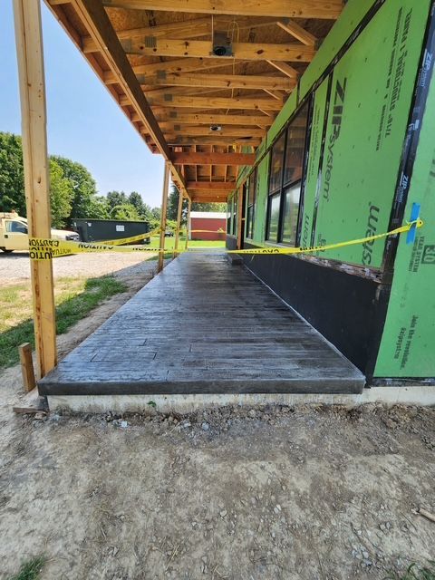 Concrete porch under construction, with wooden supports and green wall siding. Yellow caution tape present.