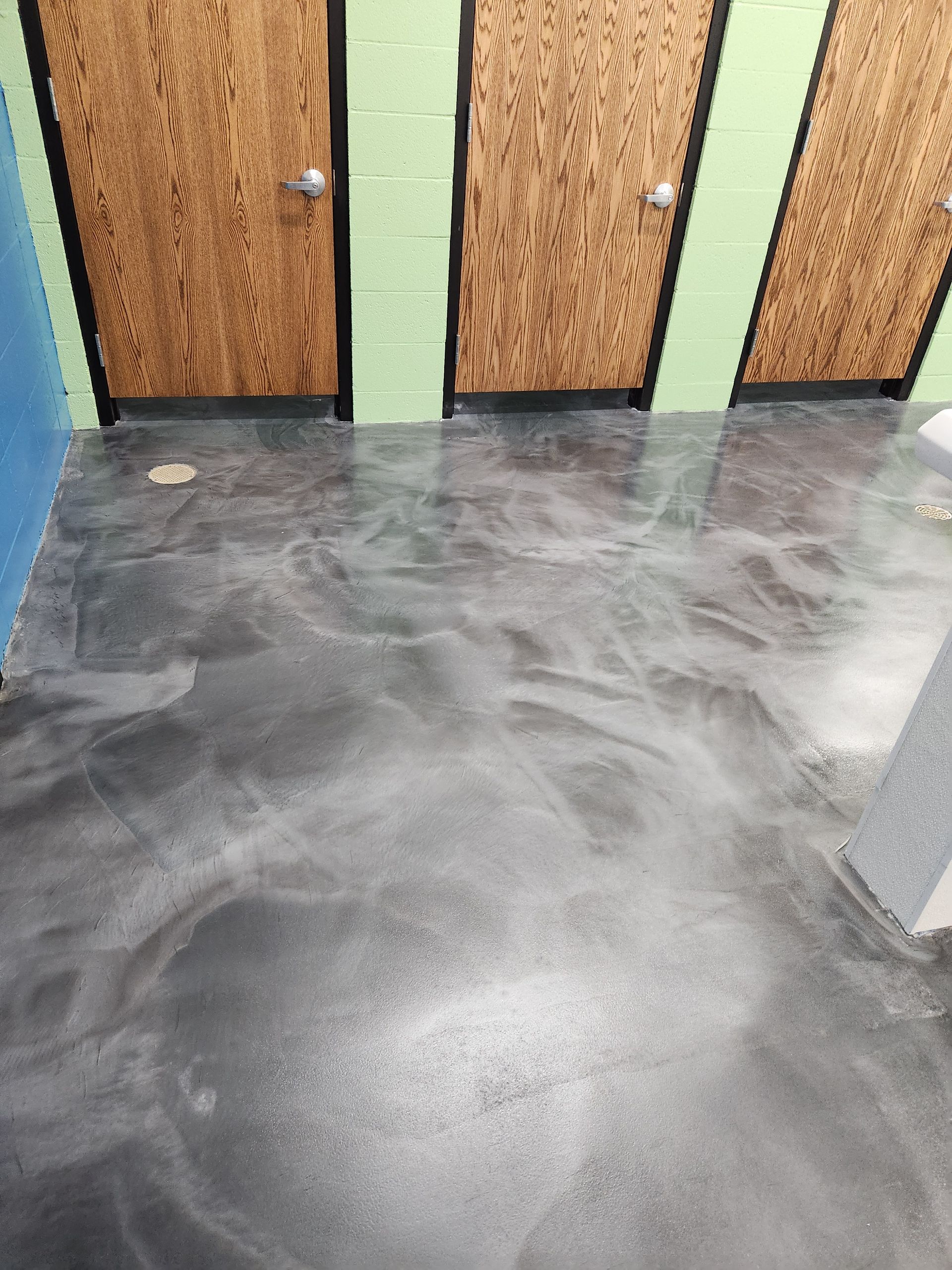 Silver epoxy flooring in a room with three wooden doors. Green and blue walls visible.