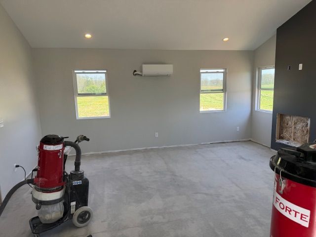 Empty room with light gray walls, windows, concrete floor, and floor sander.