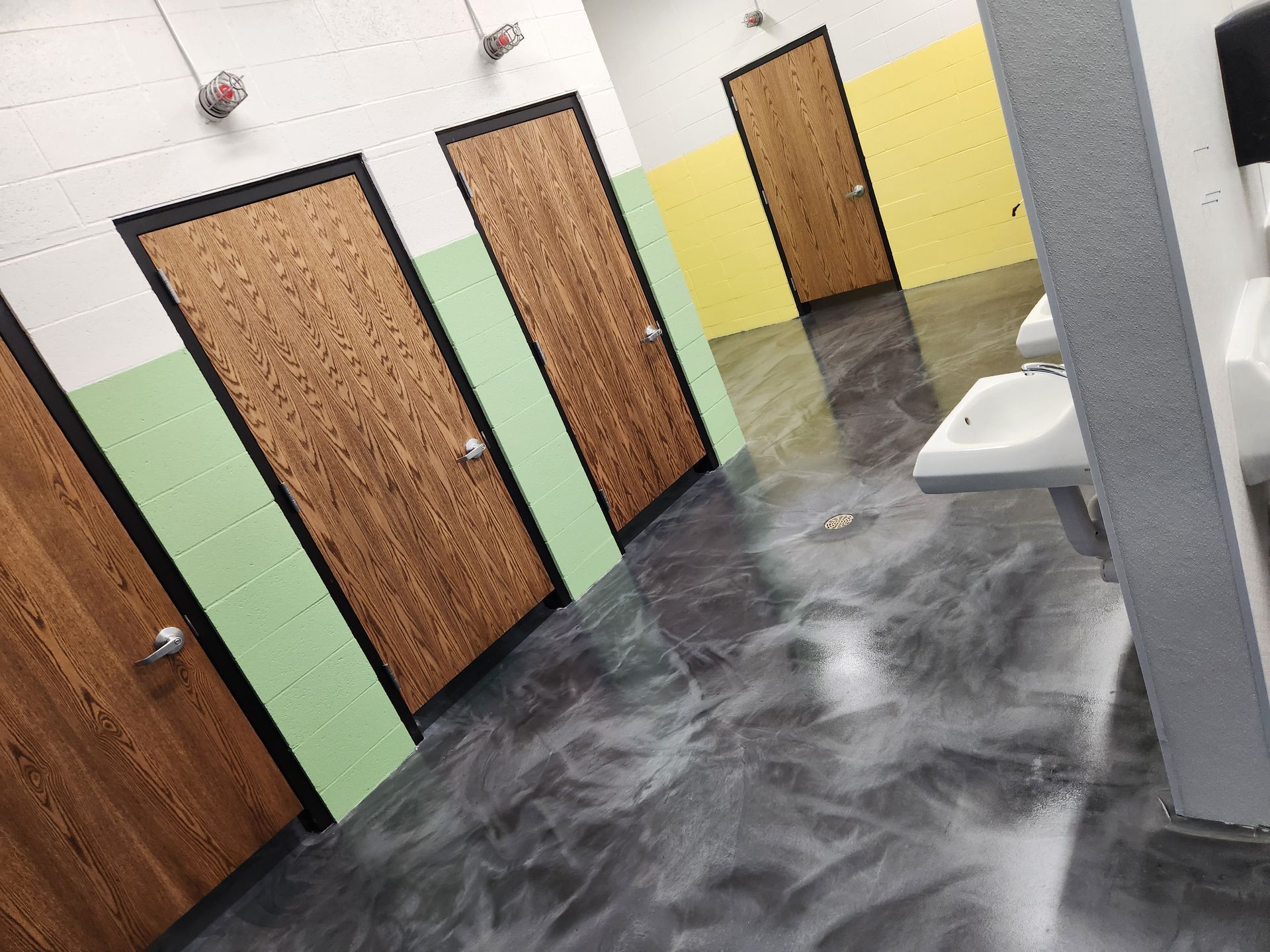 Public restroom with brown doors, green and yellow walls, and a shiny gray floor.