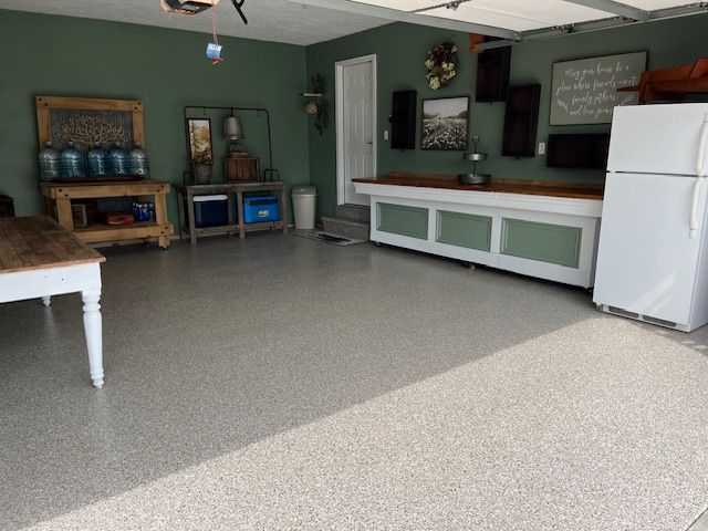 Garage interior with epoxy flooring, green walls, wooden countertops, and a white refrigerator.
