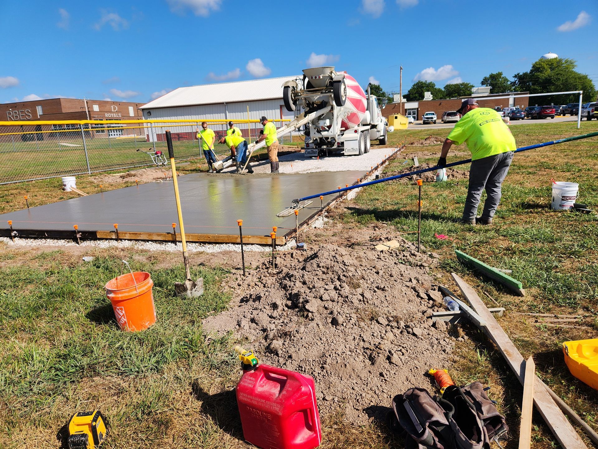 Construction workers pouring concrete slab; cement truck in background.