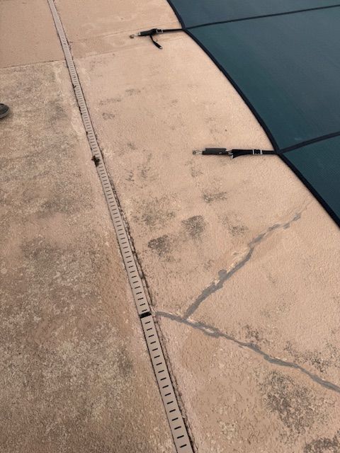 Pool deck with dark stains and a pool cover partially on top.