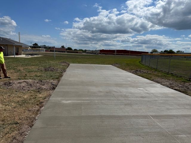 Newly poured concrete walkway in a grassy area, with a person standing on the left.