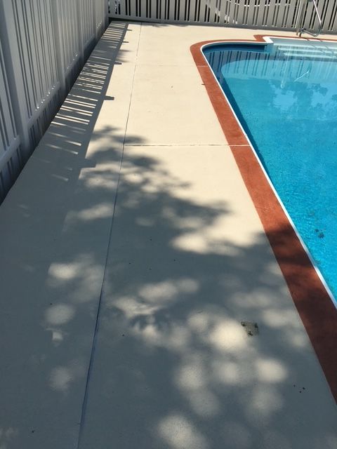 Poolside concrete patio with white fence and pool. Sunlight casts shadows on the light-colored surface.