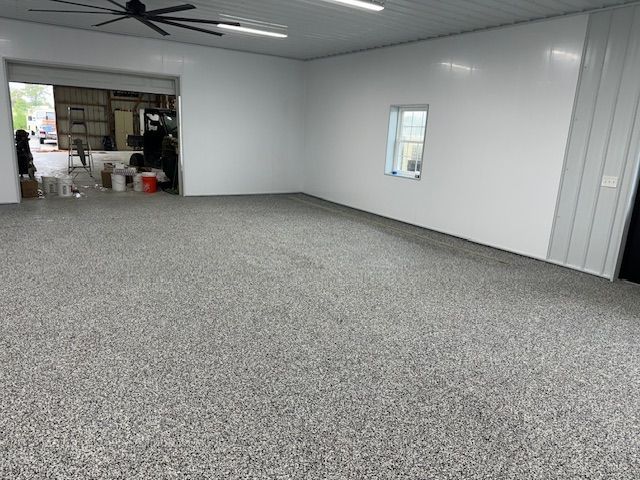 Empty, bright garage interior with gray speckled floor, white walls, large open door, and small window.