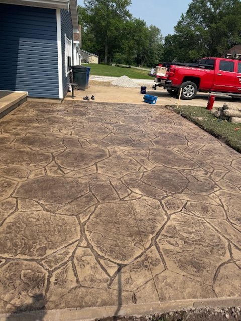 Stamped concrete patio in brown stone pattern next to blue house and red truck.