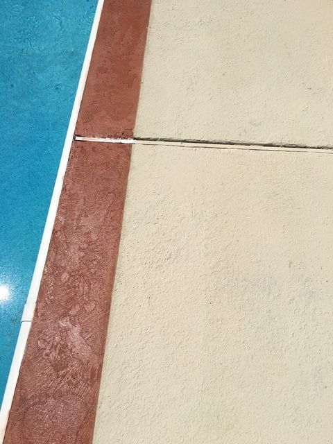 Poolside with blue water, beige concrete, and red-brown trim; a narrow crack runs through the concrete.