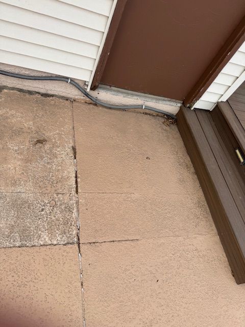 Concrete ground with cracks, gray cables along a brown wall and white siding.