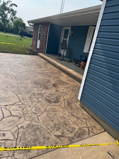 Concrete driveway with stone pattern in front of blue house with porch. Yellow caution tape.