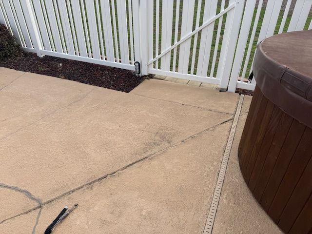 Concrete patio with cracks, white fence, hot tub.