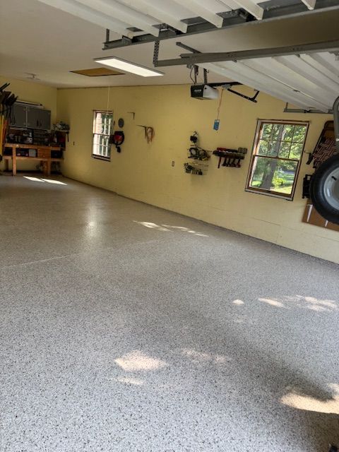 Empty garage with speckled gray floor and yellow walls. Tools and windows are visible.