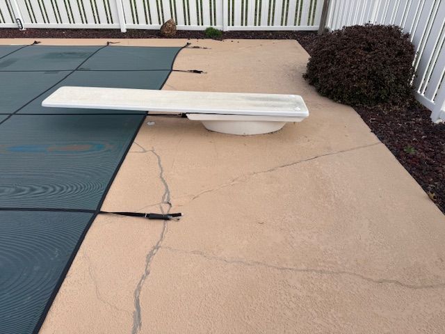 Poolside with diving board, partial pool cover, and cracked concrete.