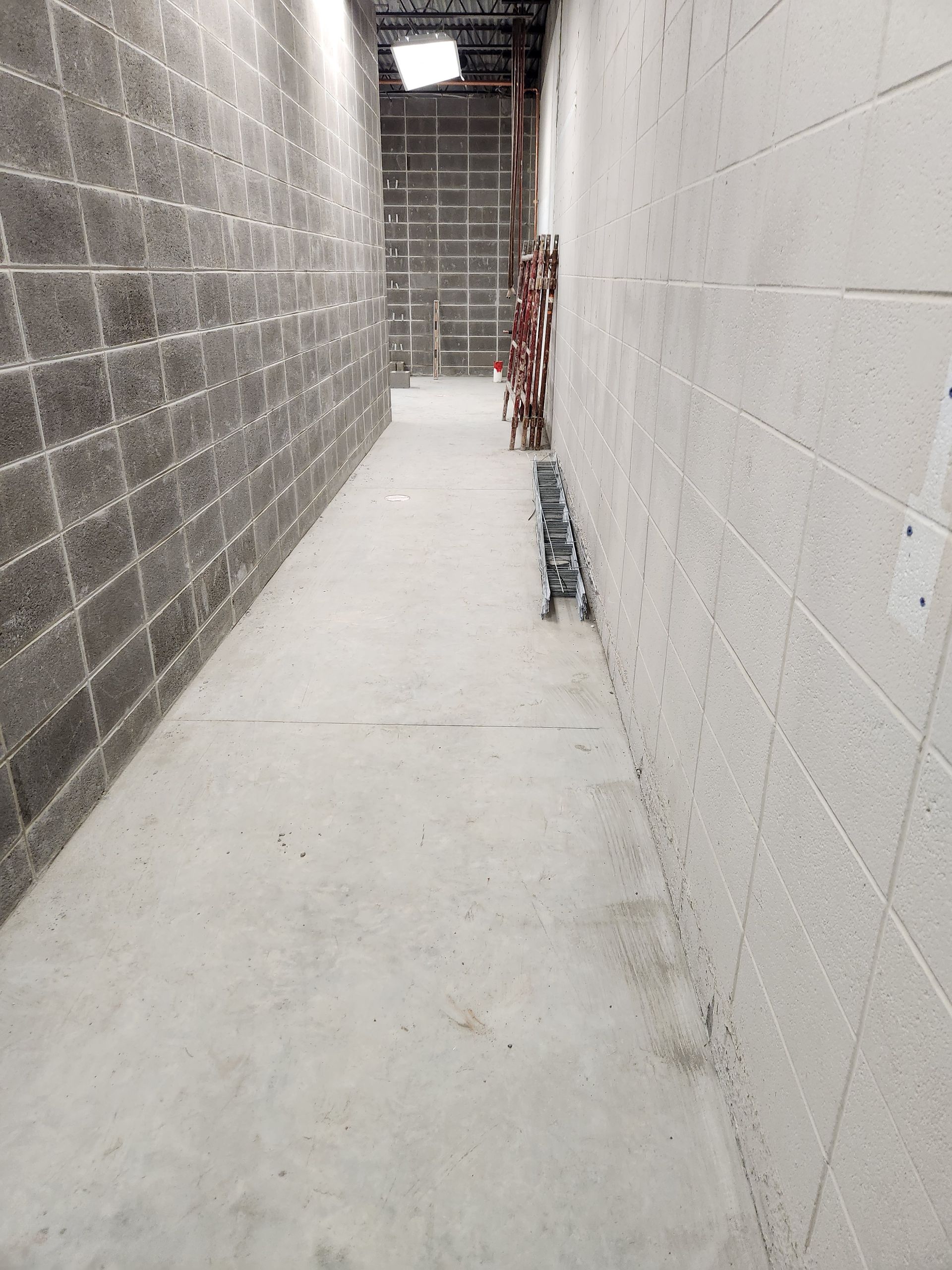 Narrow concrete hallway with cinder block walls, leading to a bright opening.
