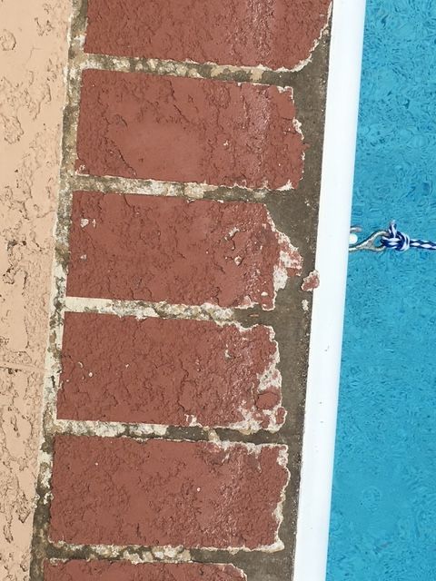 Red brick edge of a pool with white border, tan wall, and turquoise water.