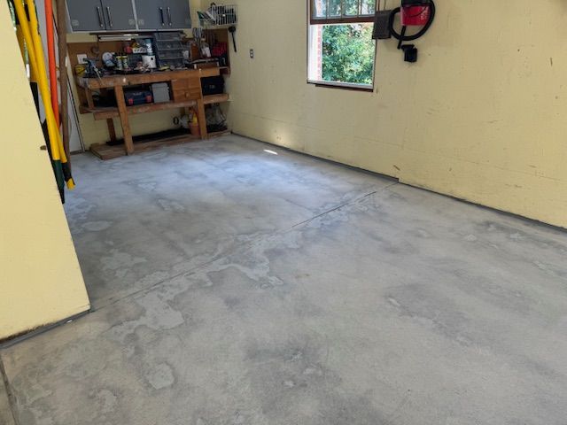 Garage interior with concrete floor, workbench, and window. Yellow walls, tools visible.