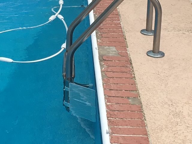 Swimming pool with metal ladder, blue water, and brick coping.