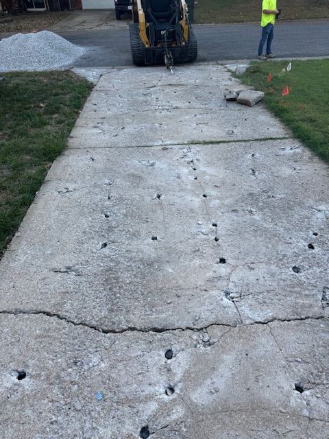 Damaged concrete driveway with holes, a small bulldozer in the background, and a worker standing nearby.