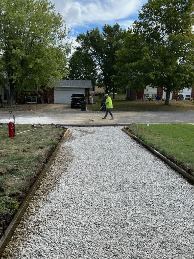 Person blowing leaves off a gravel path in front of homes.