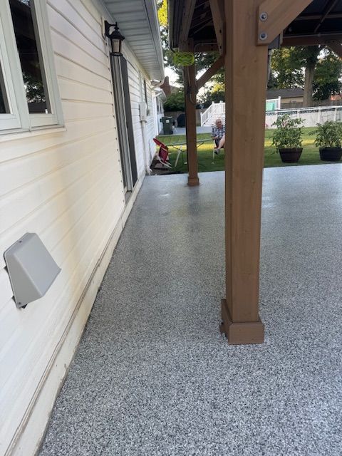 Gray speckled epoxy patio next to white house, under wooden deck. A person is visible in the background.