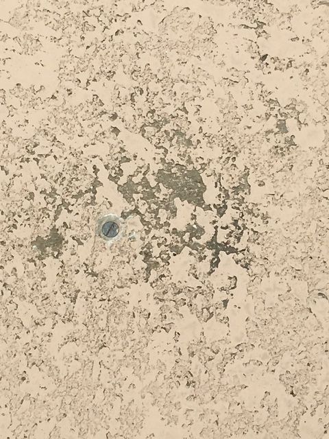 Light-colored, textured surface with chipped paint, showing a circular, recessed, dark area in the center.