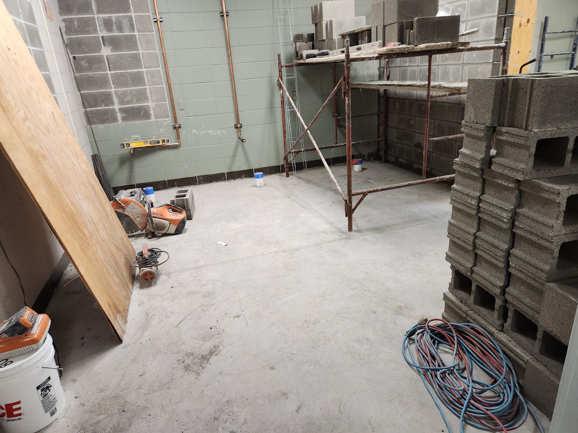 Construction site interior with concrete blocks, scaffolding, tools, and a wooden board.