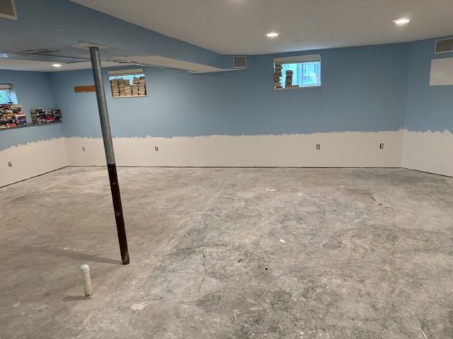 An unfinished basement with blue and white painted walls, concrete floor, and a support beam.