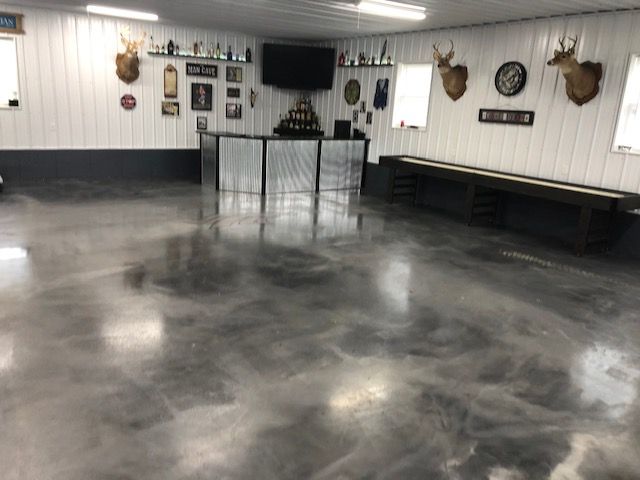 Garage with shiny, gray epoxy floor; bar area, shuffleboard table, and mounted deer heads.