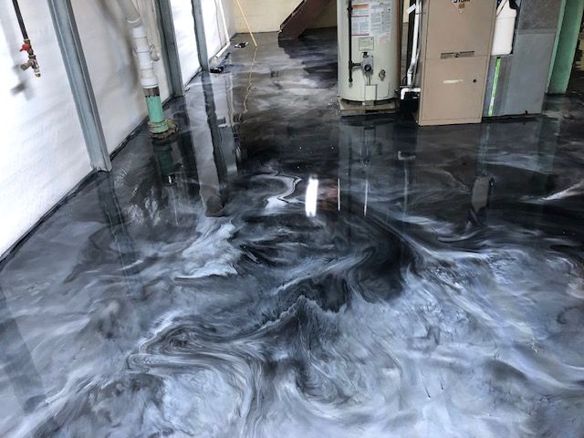 Shiny, marbled epoxy floor in shades of black, gray, and white. Basement setting with utilities visible.