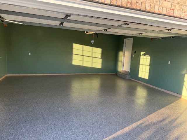 Empty garage interior with green walls and gray speckled floor; sunlight streams through windows.