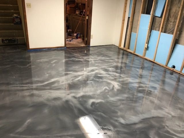 Epoxy floor with swirled gray and white patterns in a basement. Doorway and unfinished wall visible.