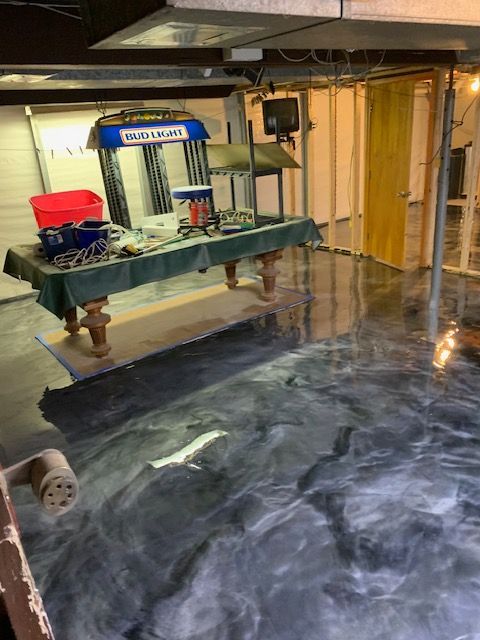 A finished basement with a metallic epoxy floor and pool table, surrounded by unfinished walls.