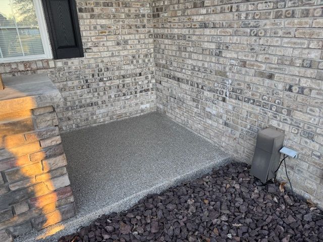 A small, gray speckled concrete porch area with a brick wall and dark rocks.