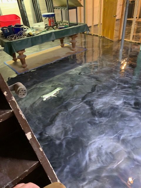 Epoxy floor in dark blue and silver tones, reflecting light. Staircase and pool table in the background.