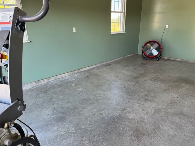Concrete floor in a room, with green walls and a fan. A machine is on the left.