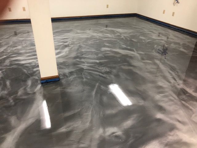 Metallic epoxy floor with gray and white swirls in a room, reflecting overhead lights.