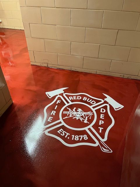 Red epoxy floor with white Red Bud Fire Dept logo. Brick wall in background.