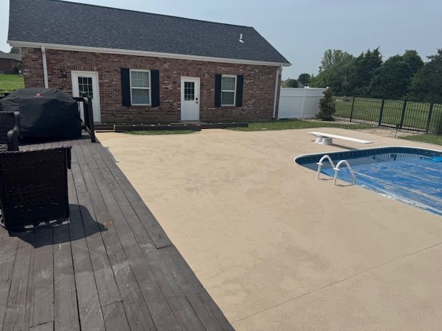 Backyard with a deck, concrete patio, pool, and brick building with black shutters.