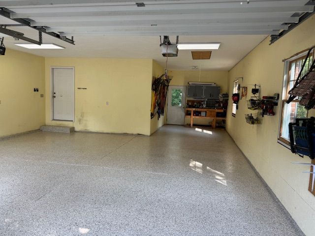 Spacious garage with epoxy floor and light yellow walls. Workshop area with tools and door. Sunlight streams in.