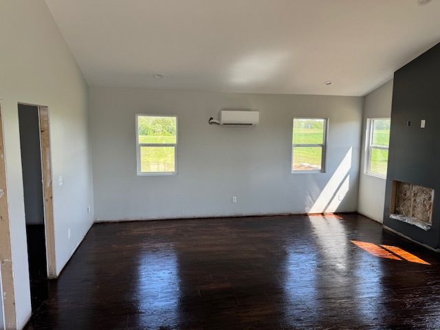 Empty room with dark wood floor, gray walls, three windows, and a dark fireplace.