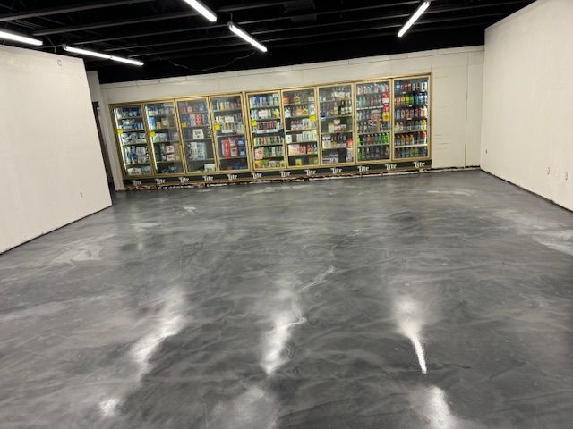 Empty room with shiny gray floor and glass display cases filled with products along one wall.